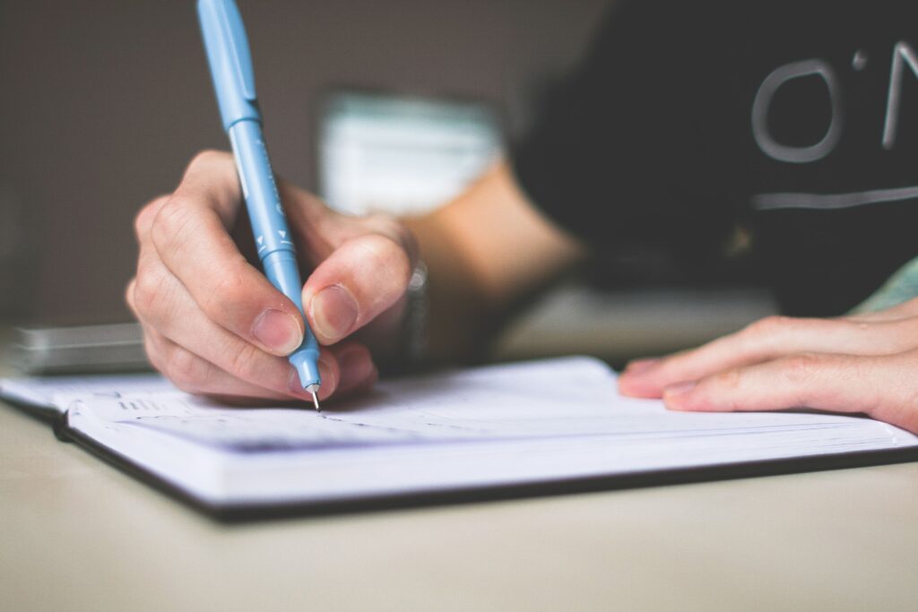Persona sosteniendo un boligrafo azul escribiendo en un cuaderno